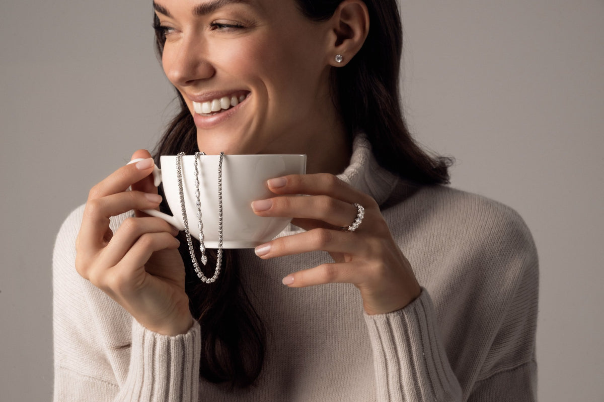 Hände in Kaschmir mit Kaffeetasse und Diamantschmuck