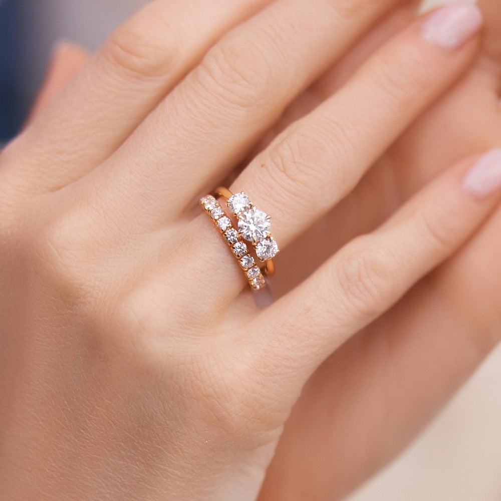 Hand mit Dreistein-Verlobungsring und Diamant-Ehering in 18k Gelbgold